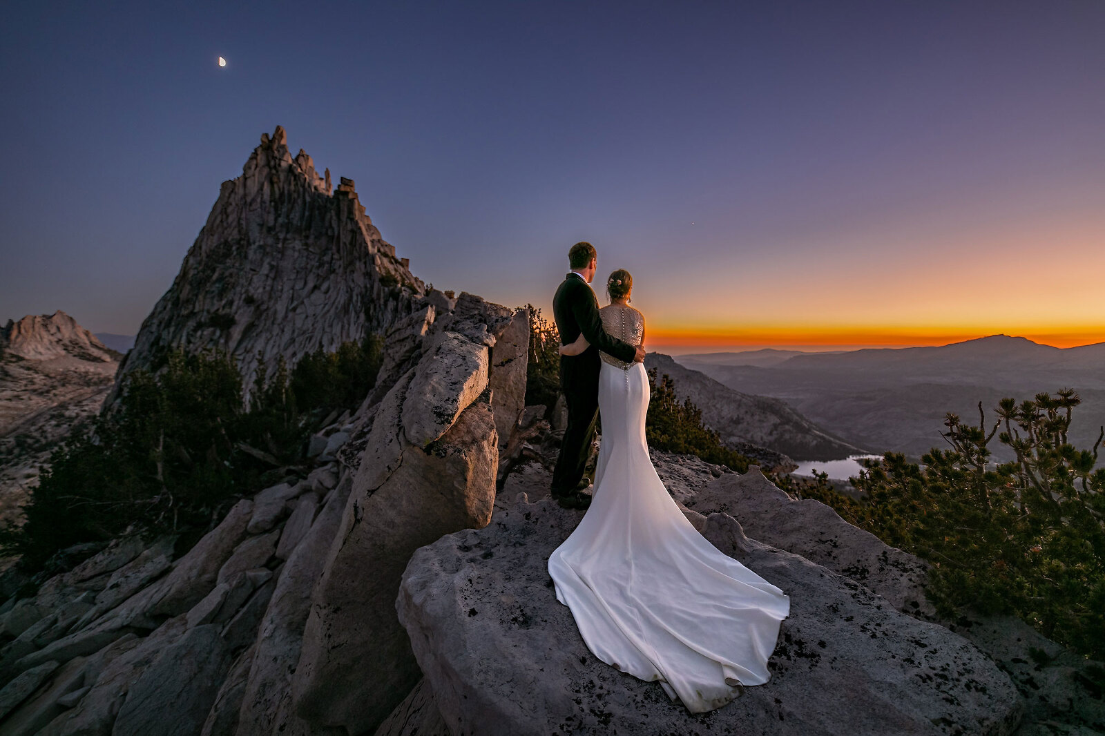 Wedding couple on mountain peak watching sunset with moon