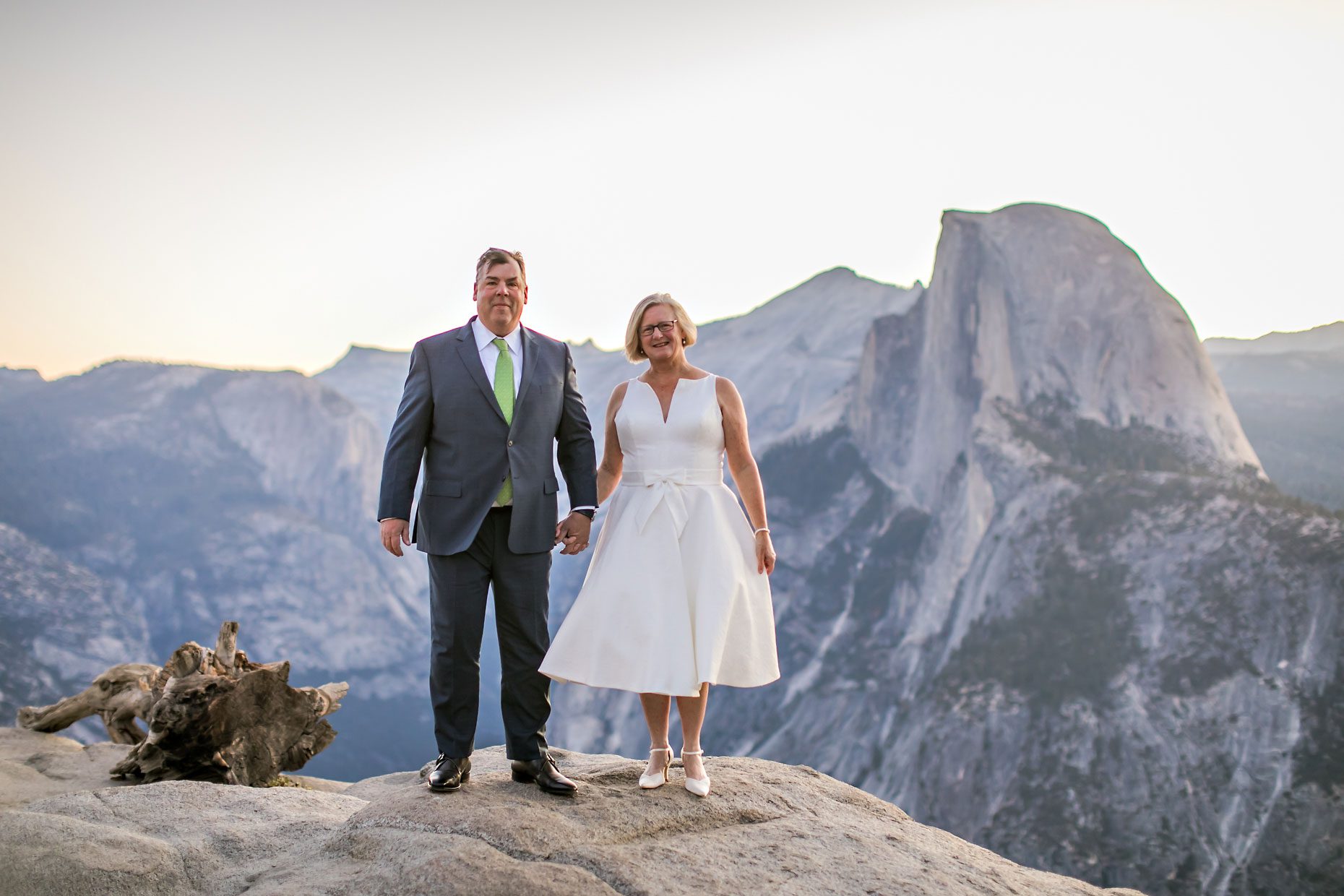 Couple gets wedding photography in Yosemite National Park at Glacier Point at sunrise with moon in background.