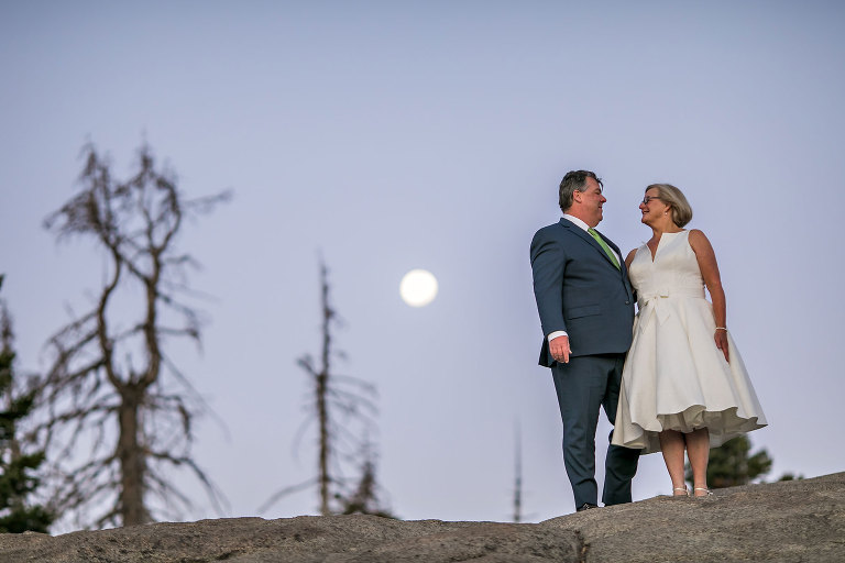 Couple gets wedding photography in Yosemite National Park at Glacier Point at sunrise with moon in background.