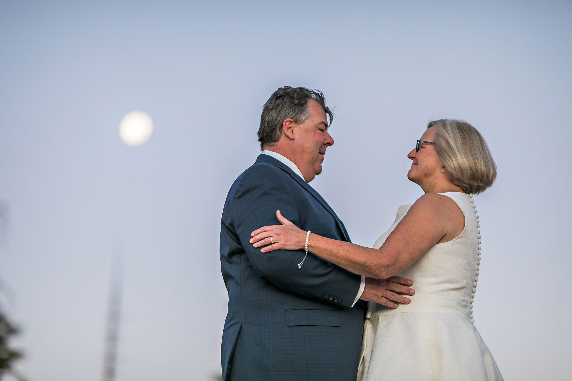 Couple gets wedding photography in Yosemite National Park at Glacier Point at sunrise with moon in background.