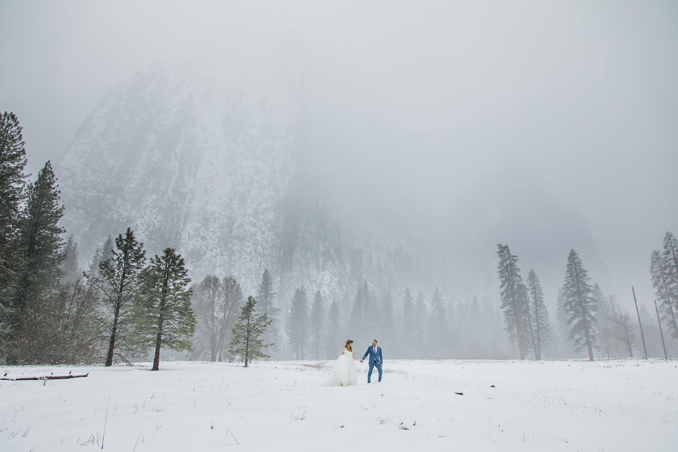 Bride and Groom walking in meadow in winter with mountains.