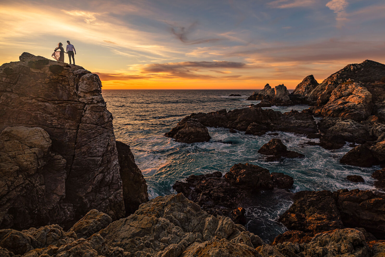 A elopement couple standing on a rock at the ocean watching the sunset