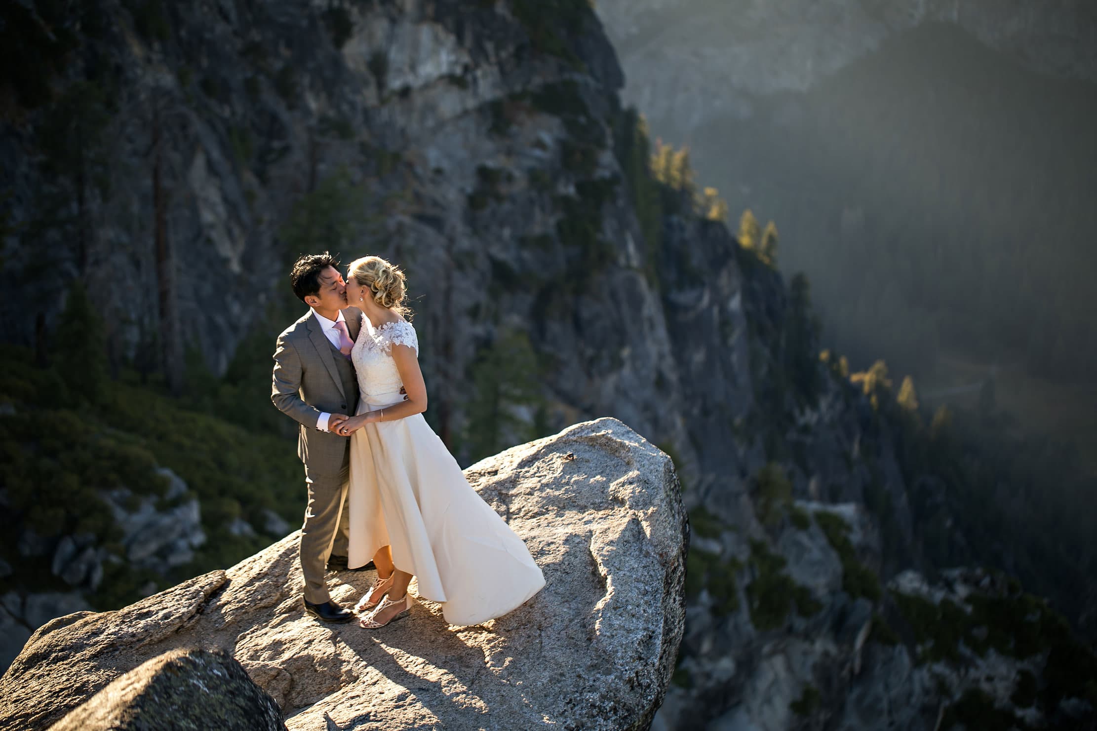 Bride and Groom kissing on a cliff edge in the mountains.