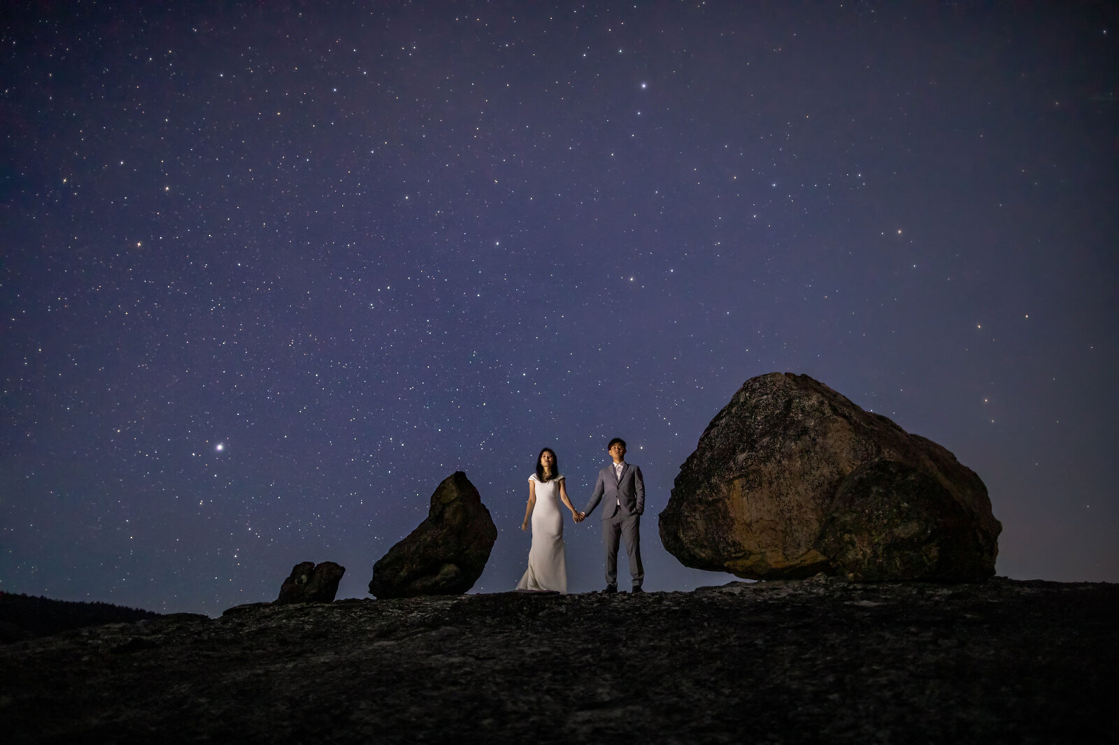 Bride and Groom standing on a mountain with boulders underneath the stars