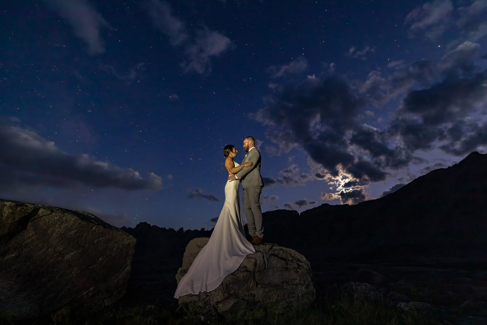 A wedding couple standing on mountain underneath the stars and moon.