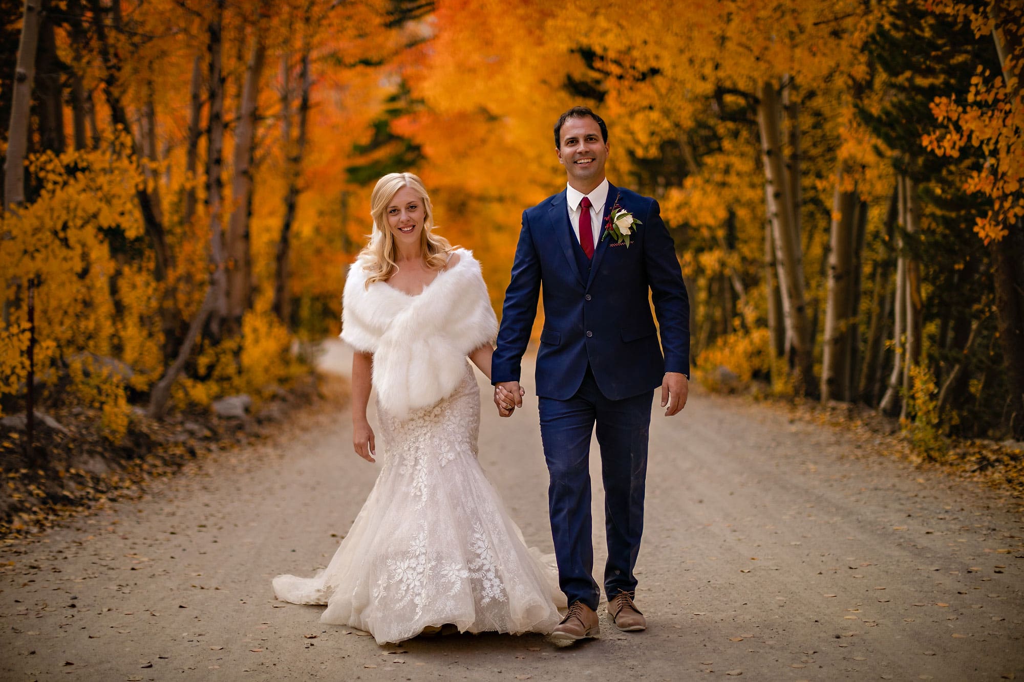 Bride and groom walking a dirt road during peak fall colors.