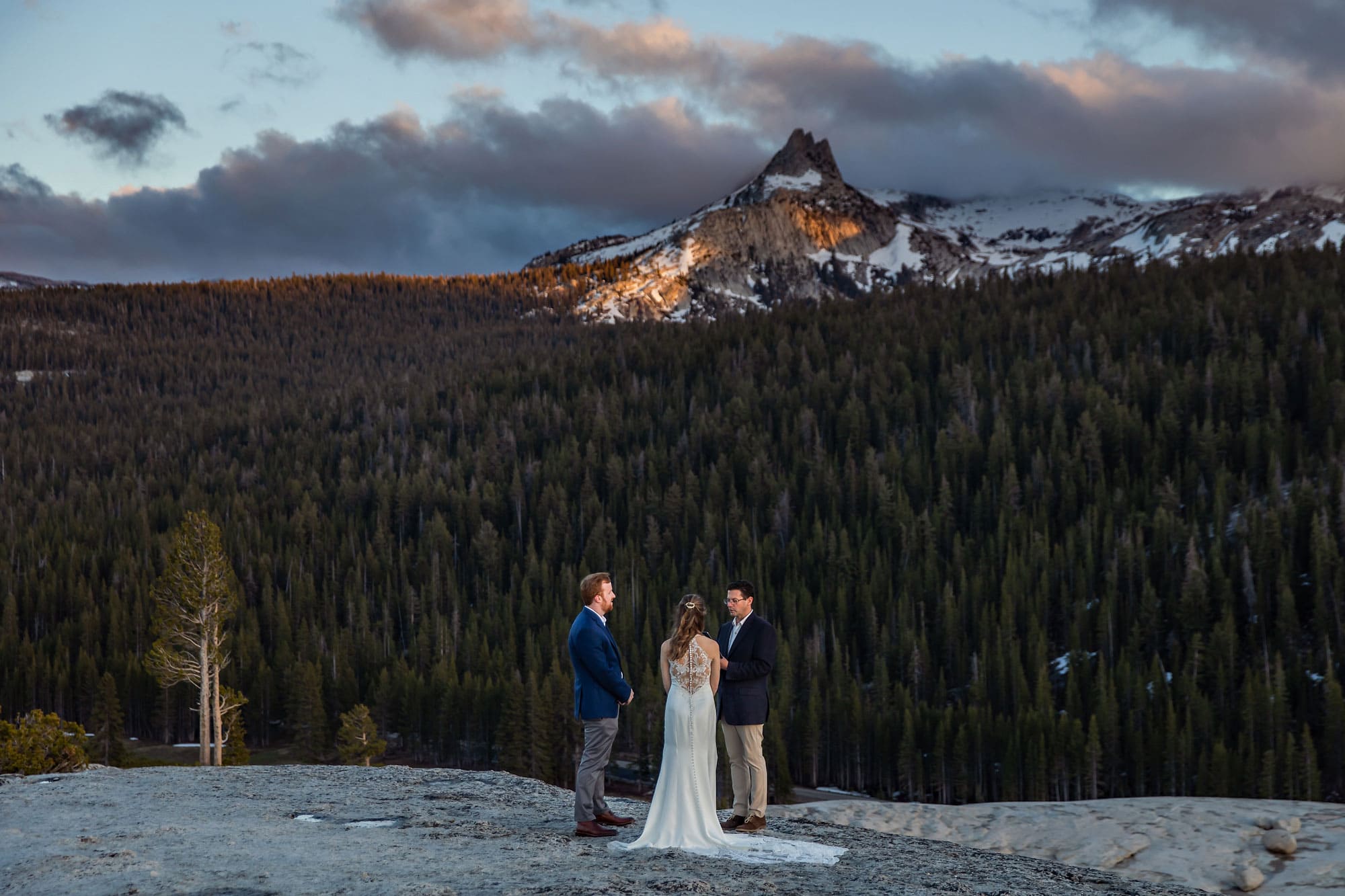 A Bride and Groom getting married on top of mountain during sunset.
