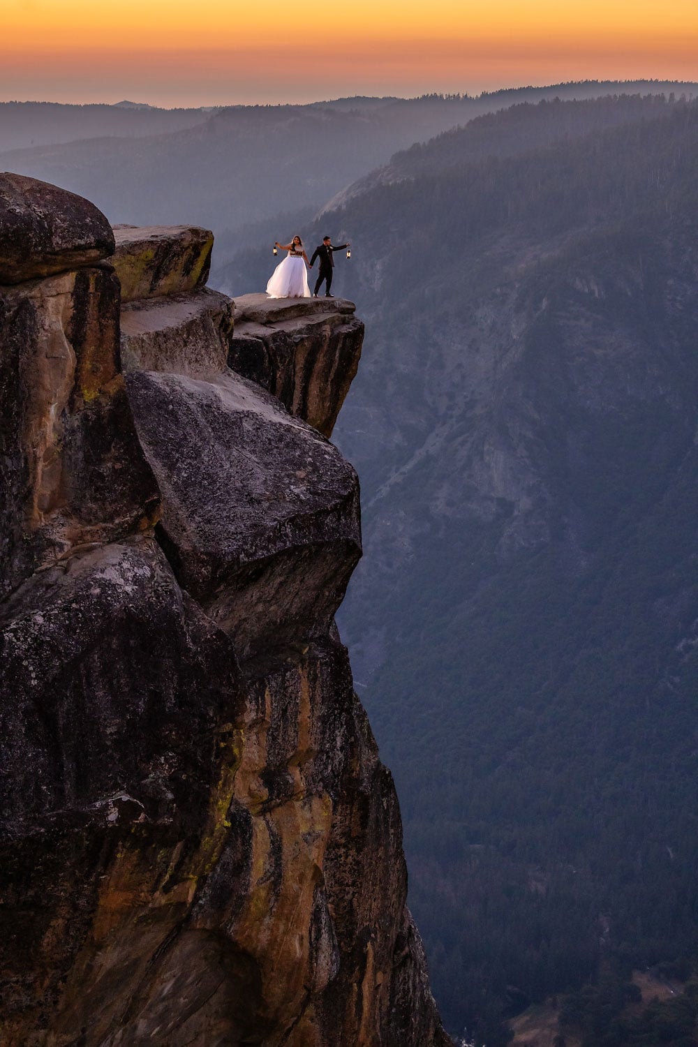 Indigenous mixed wedding couple on the edge of a cliff with lanterns during sunset light.