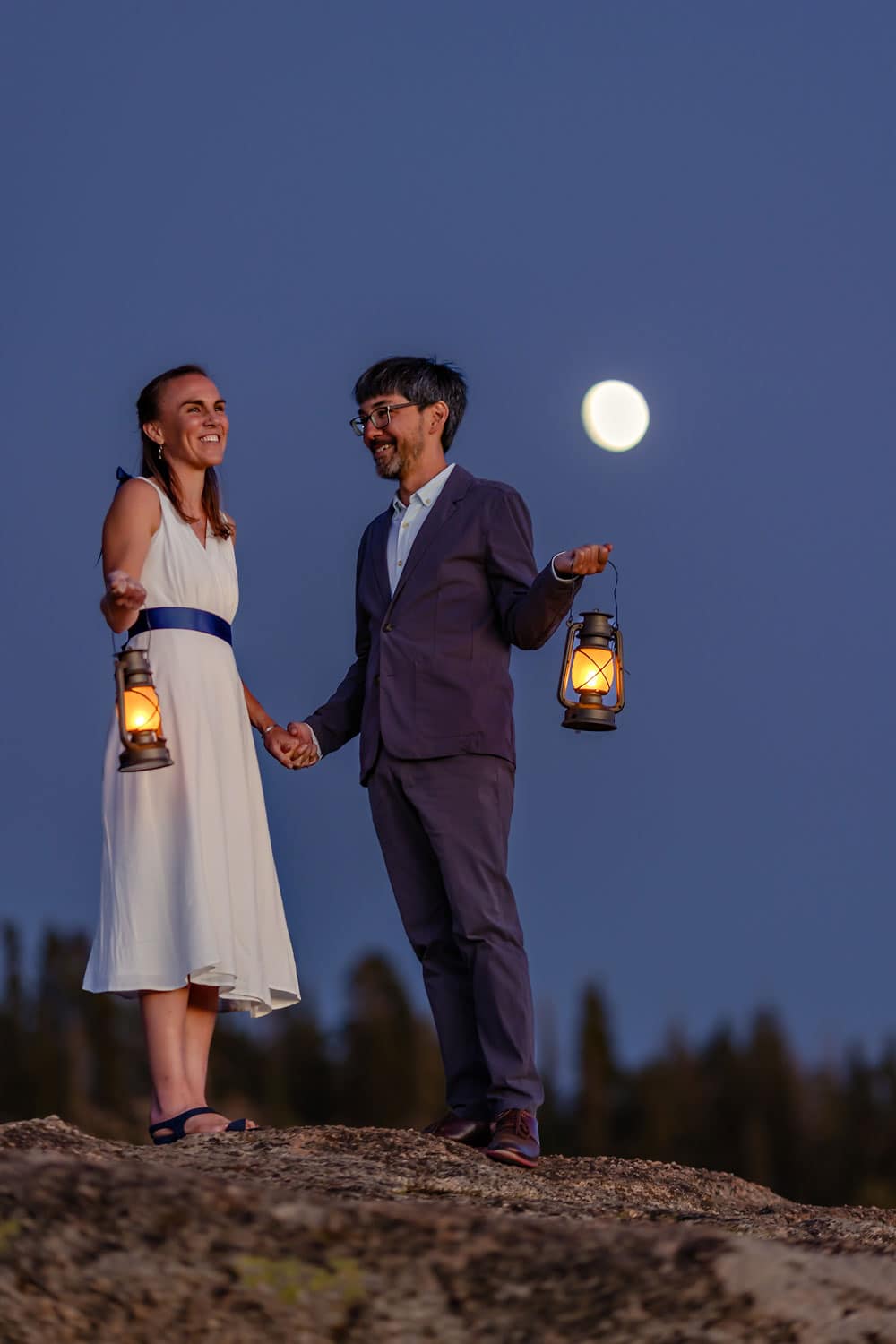 A Bride and Groom standing on top of boulder underneath the stars and moon light with lanterns,