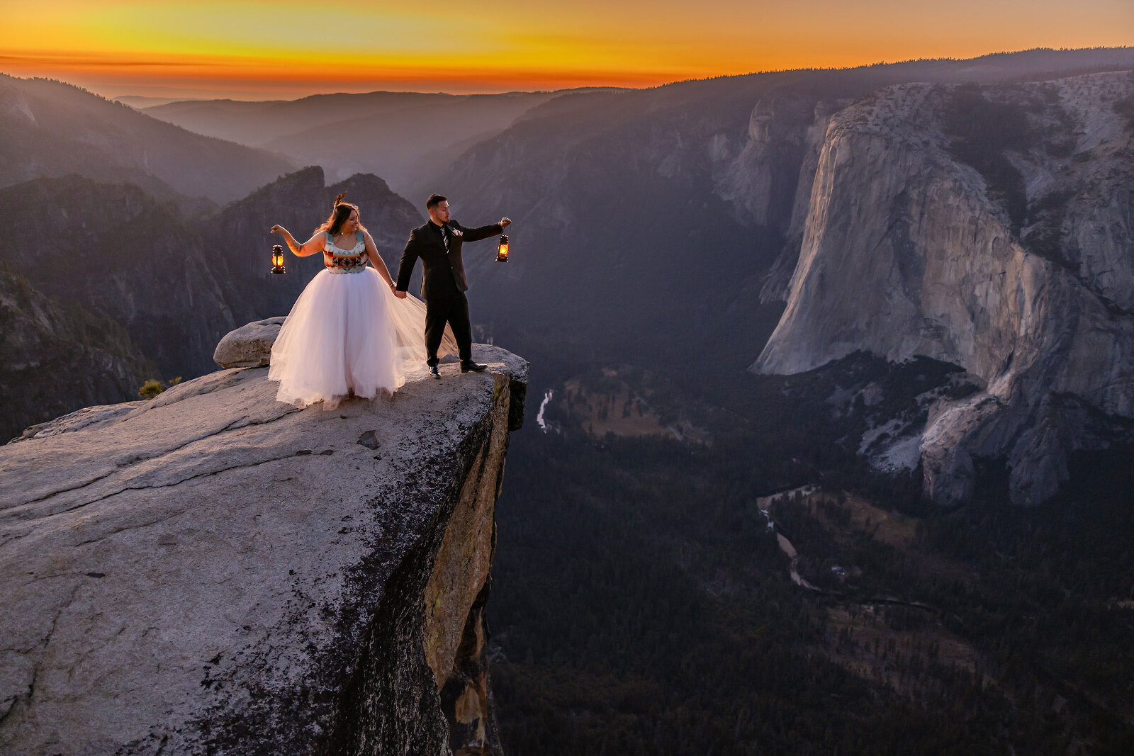 Indigenous mixed wedding couple on the edge of a cliff with lanterns during sunset light.